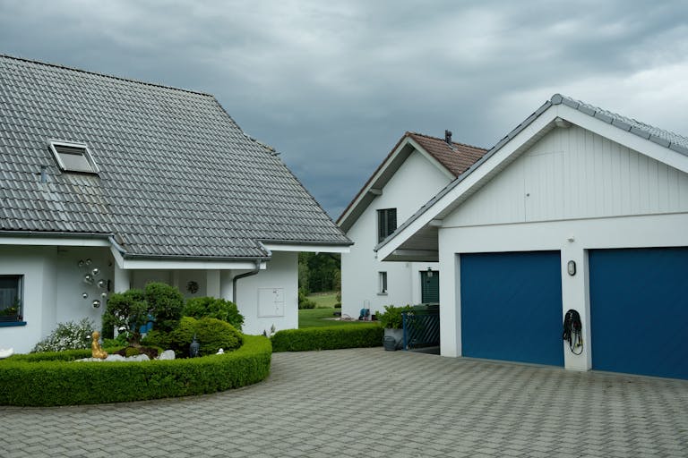 Lovely suburban houses with blue garage doors under cloudy sky, surrounded by greenery.
